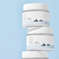 Image of ROUND LAB 1025 Dokdo Cream 80ml stacked jars with minimalist design on blue background