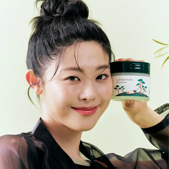 Smiling woman holding ROUND LAB Pine Calming Cica Pads 50 sheets with gentle skincare benefits.