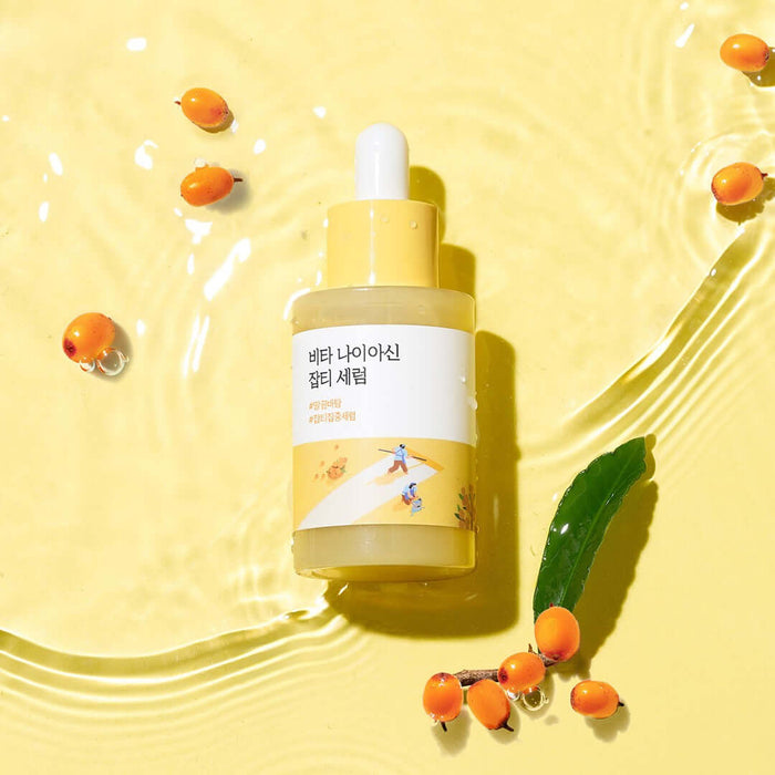 ROUND LAB Vita Niacin Spot Serum 30ml bottle on yellow surface with sea buckthorn berries and water ripples.