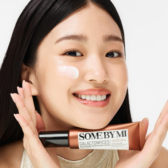 Smiling woman holding SOME BY MI Galactomyces Glutathione Brightening Cream 40ml, showcasing product application.