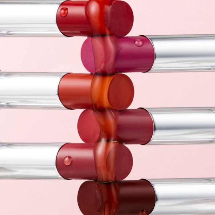 Colorful TONY MOLY Get It Tint Syrup Stick lipsticks arranged creatively against a pink background.